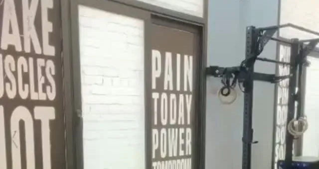 Printed slogan walls reading Make muscles not excuses and Pain today power tomorrow, beside a black rig